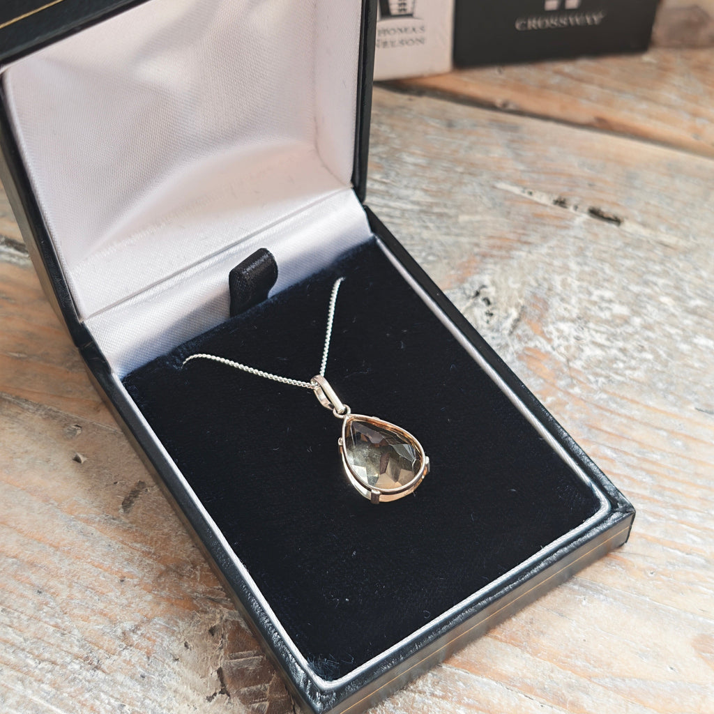 925 silver citrine pendant on a necklace with a silver chain and bezel, displayed inside an open black jewelry box on a rustic wooden surface..