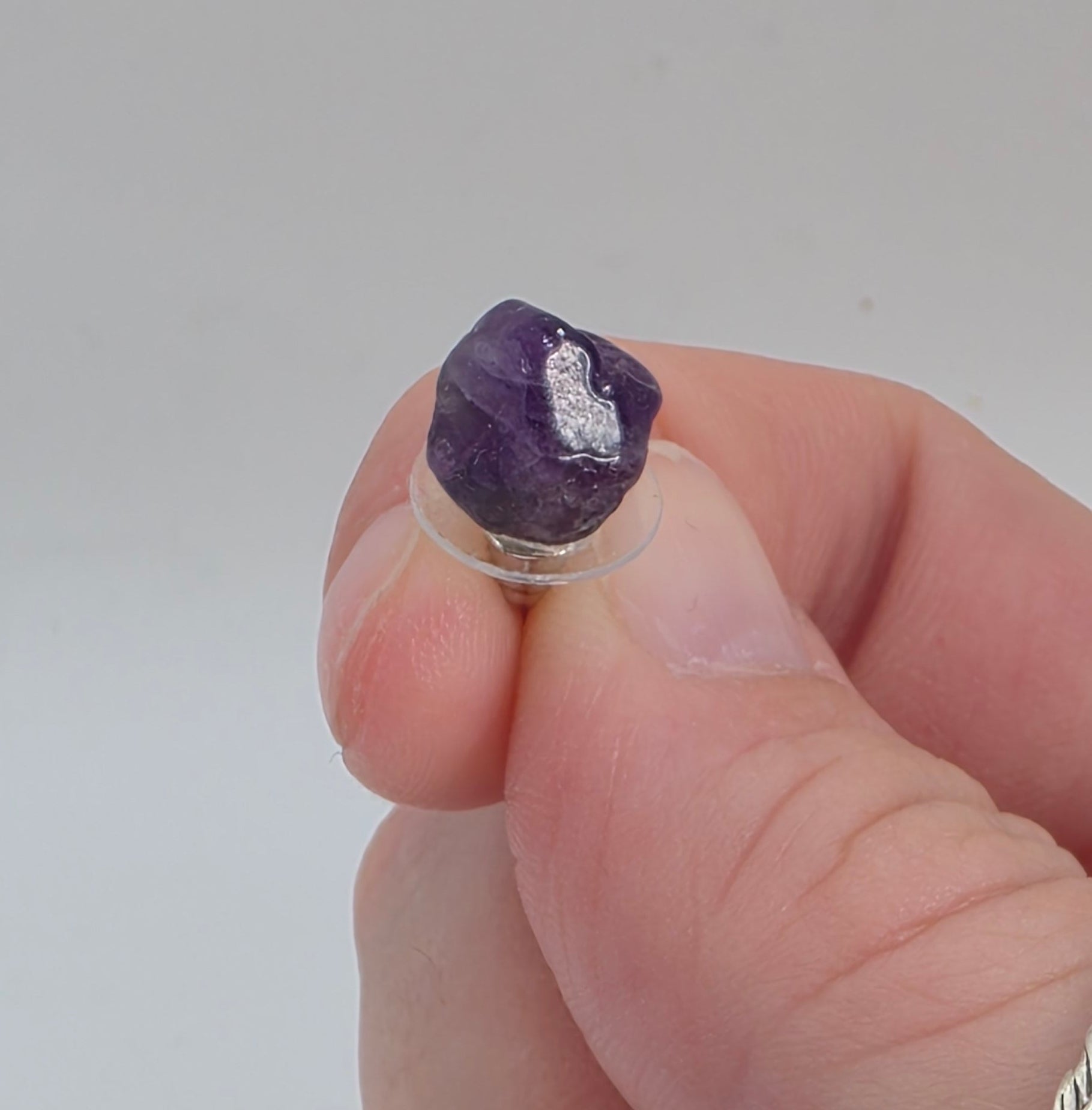 Hand holding a small Amethyst earring against a plain background