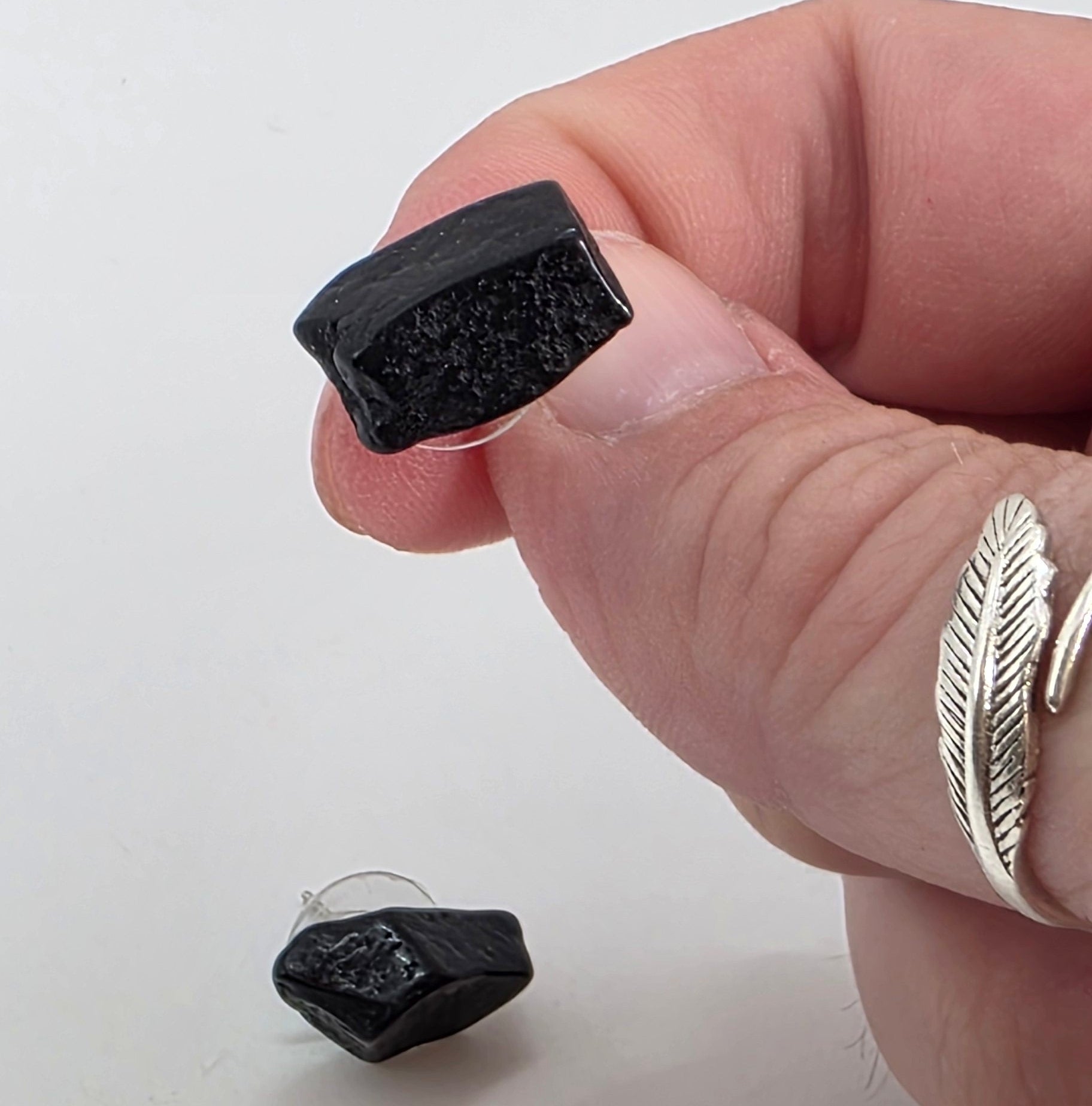 Black tourmaline earrings held between fingers on a white background