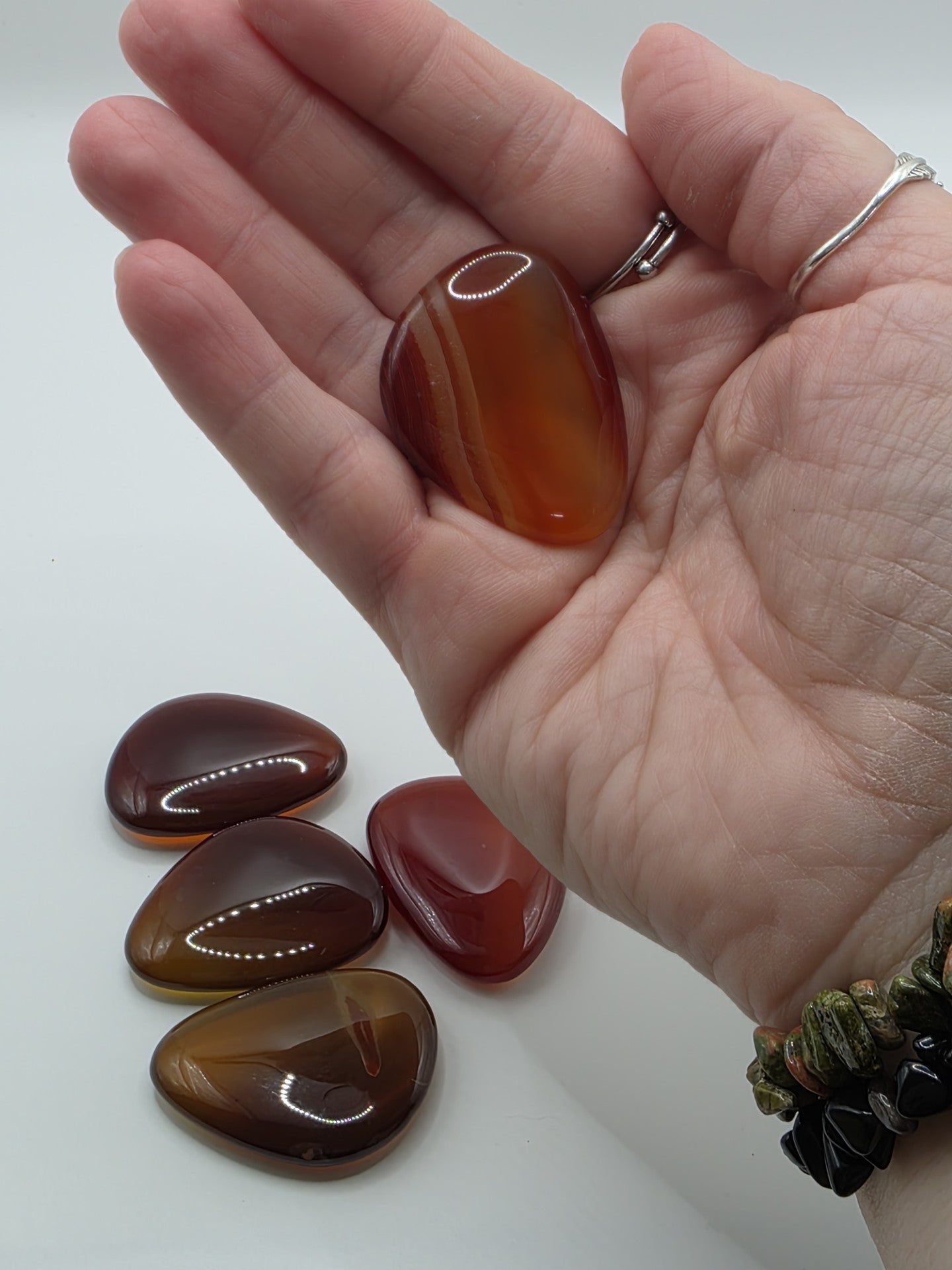 Hand holding a polished carnelian palm stone with more stones on a white background