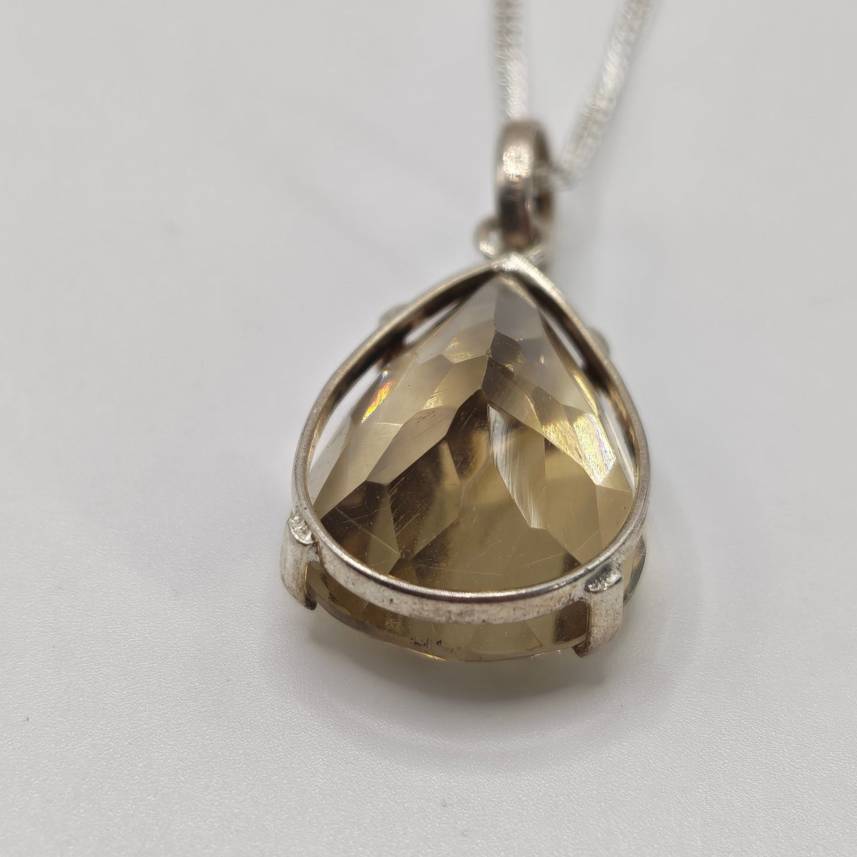 Faceted teardrop-shaped citrine gemstone pendant in a silver bezel setting on a silver chain, photographed on a light background.