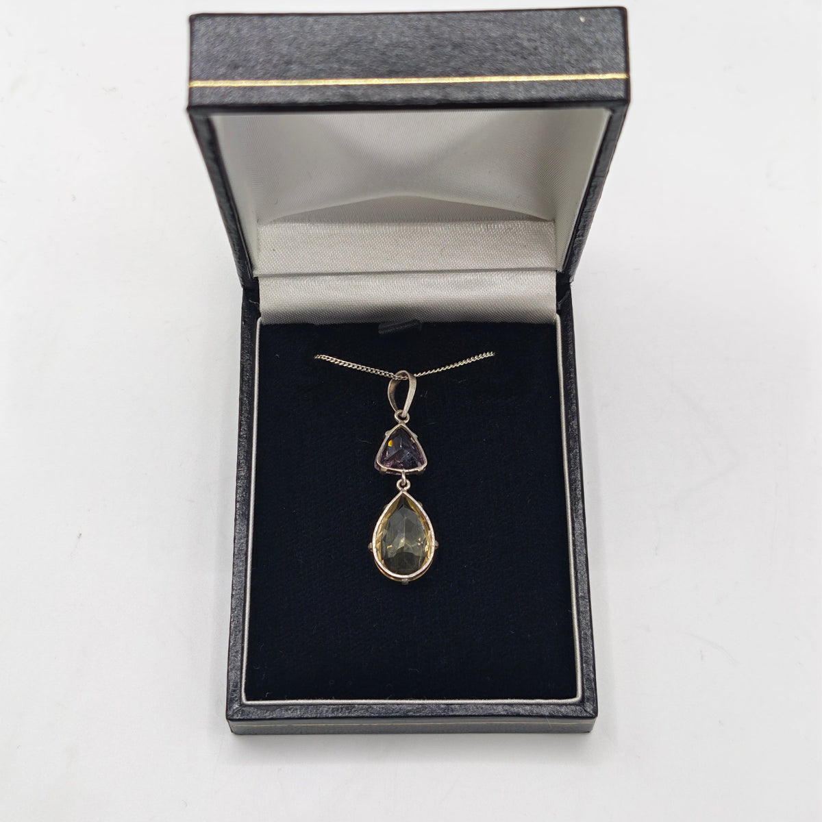 A silver pendant necklace featuring a larger citrine teardrop and a smaller triangular amethyst gemstone, in jewelry box