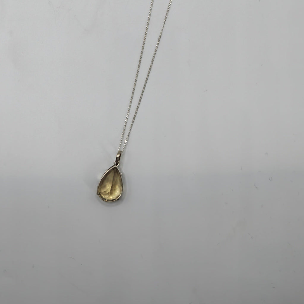 A delicate silver chain necklace with a small Citrine Faceted teardrop-shaped  gemstone pendant, displayed against a plain light  background.