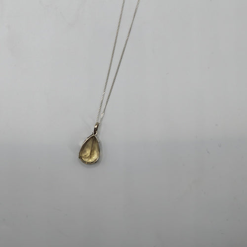 A delicate silver chain necklace with a small Citrine Faceted teardrop-shaped  gemstone pendant, displayed against a plain light  background.