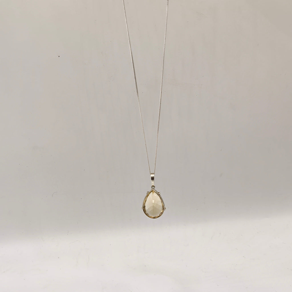 A silve teardrop citrine pendant necklace  held by a hand against a plain white background.