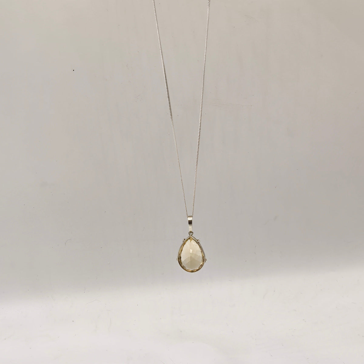 A silve teardrop citrine pendant necklace  held by a hand against a plain white background.