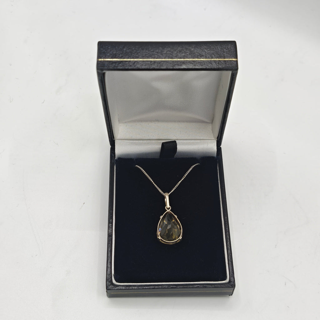 A citrine teardrop pendant necklace displayed inside an open black jewelry box on a white surface.