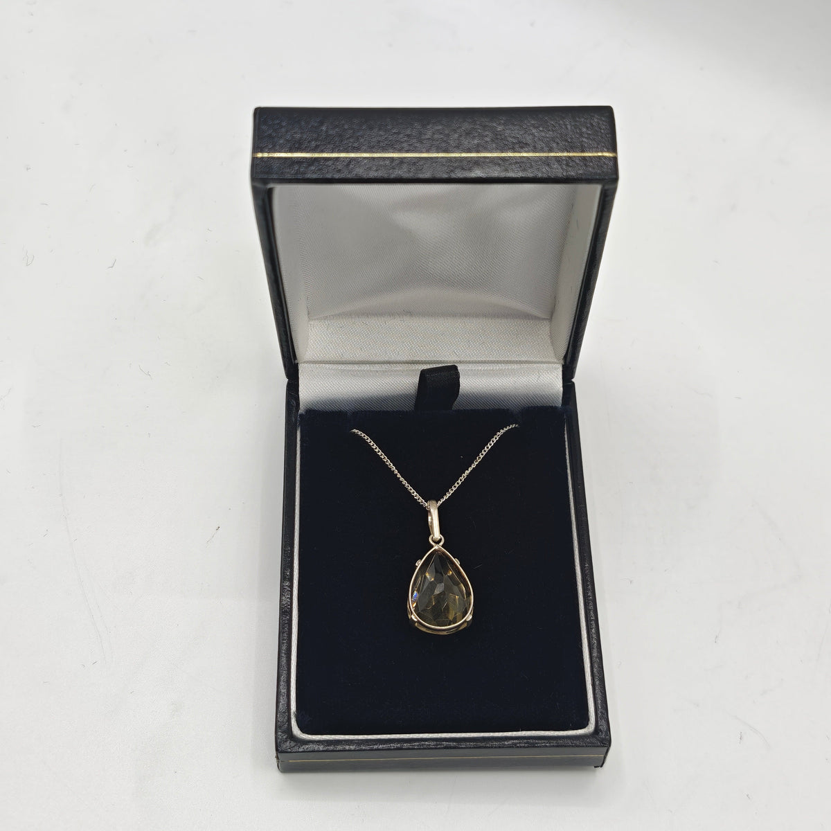 A citrine teardrop pendant necklace displayed inside an open black jewelry box on a white surface.