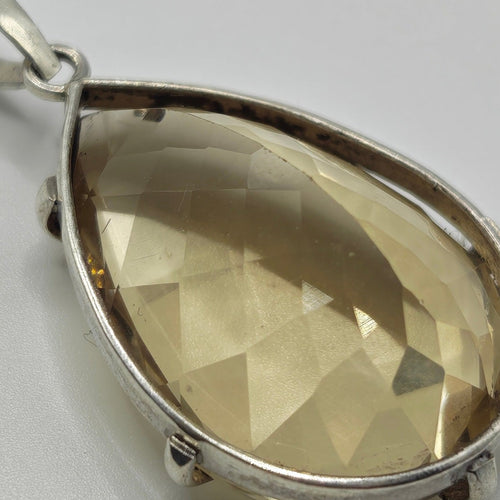 A silver pendant featuring a faceted, teardrop-shaped light yellow citrine gemstone, hand faceted, shown on a plain white background.