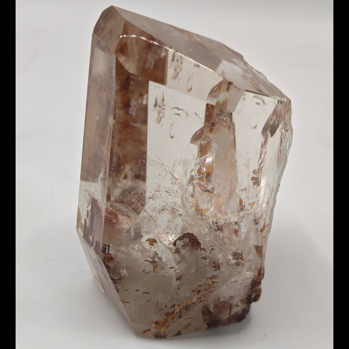 A raw, unpolished Fire quartz crystal with natural inclusions, standing upright on a neutral light gray background.