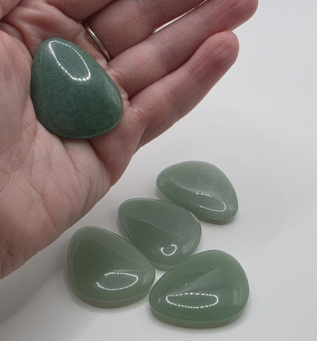 Green aventurine held in a hand with additional stones on a white surface
