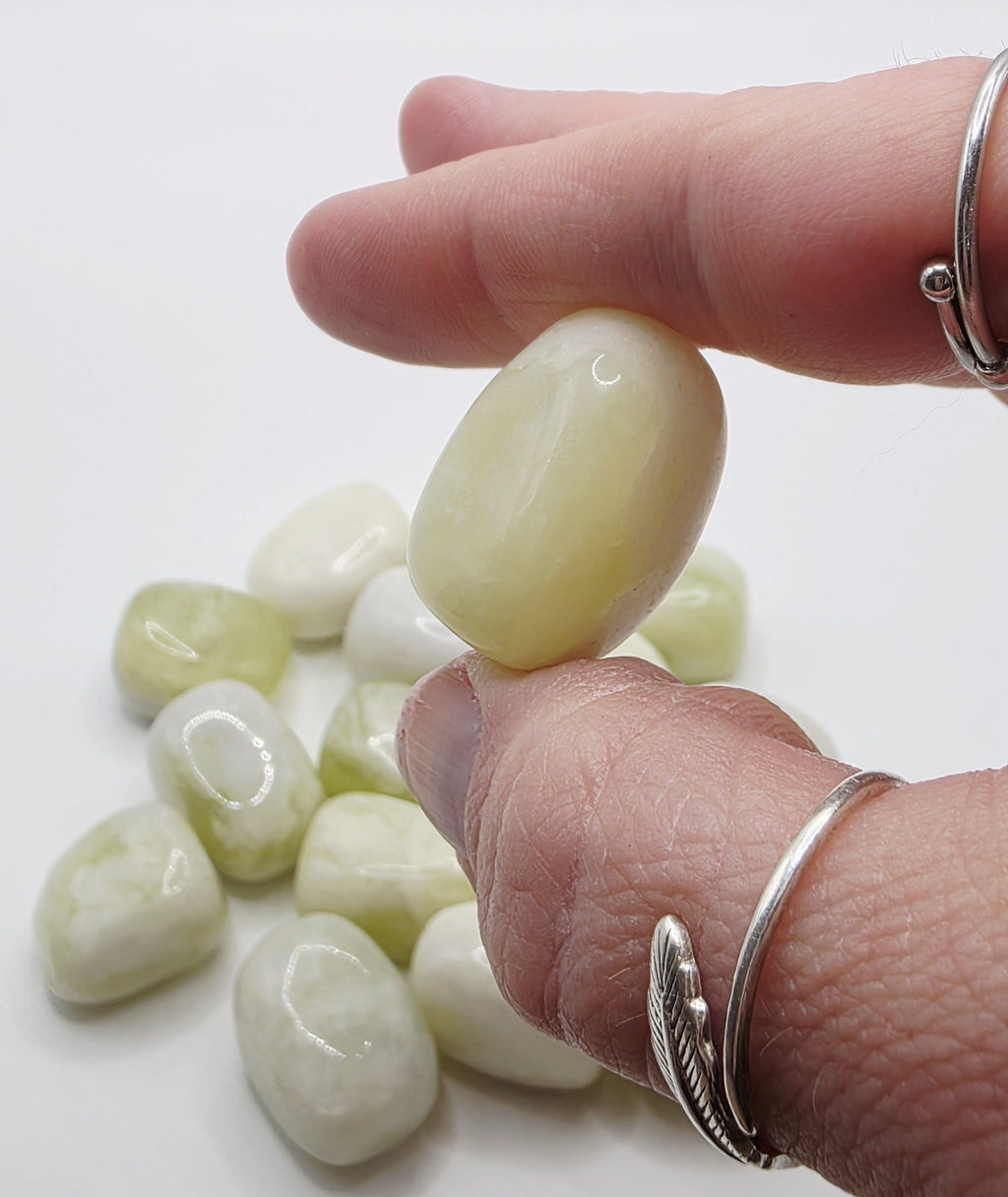 Hand holding a Jade stone with more stones on a white background