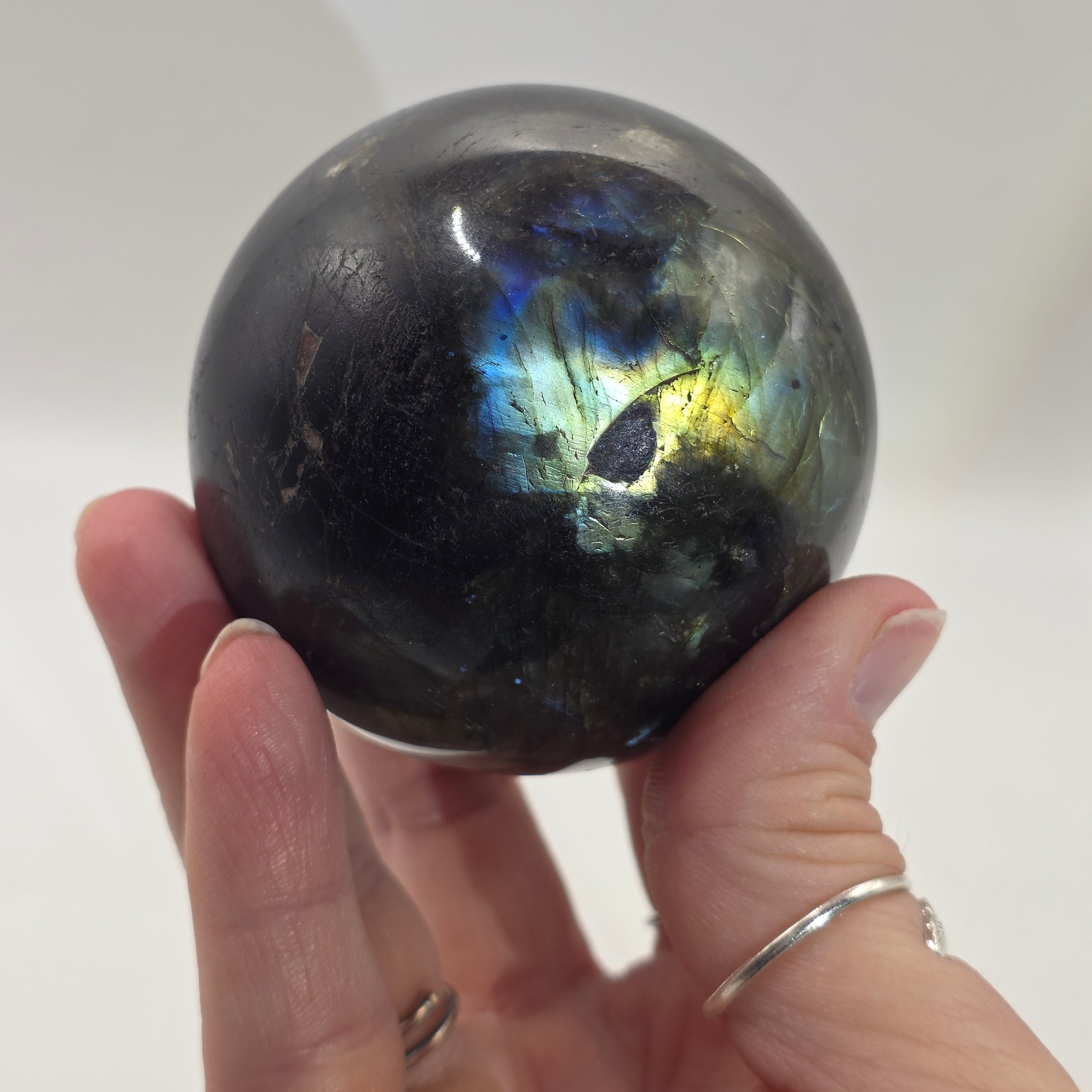 Hand holding a labradorite crystal sphere against a white background