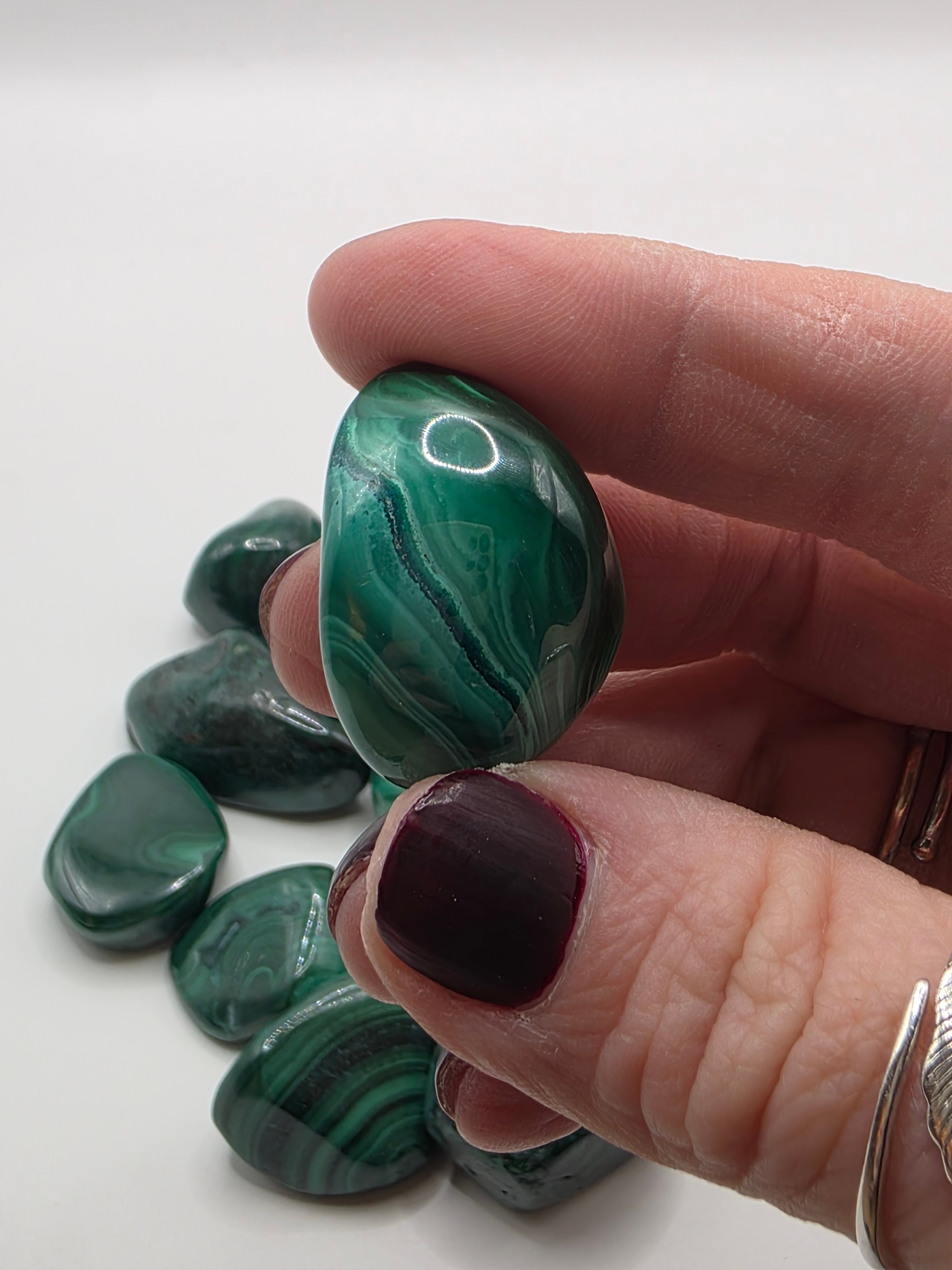 Hand holding a malachite stone with more stones on a white background