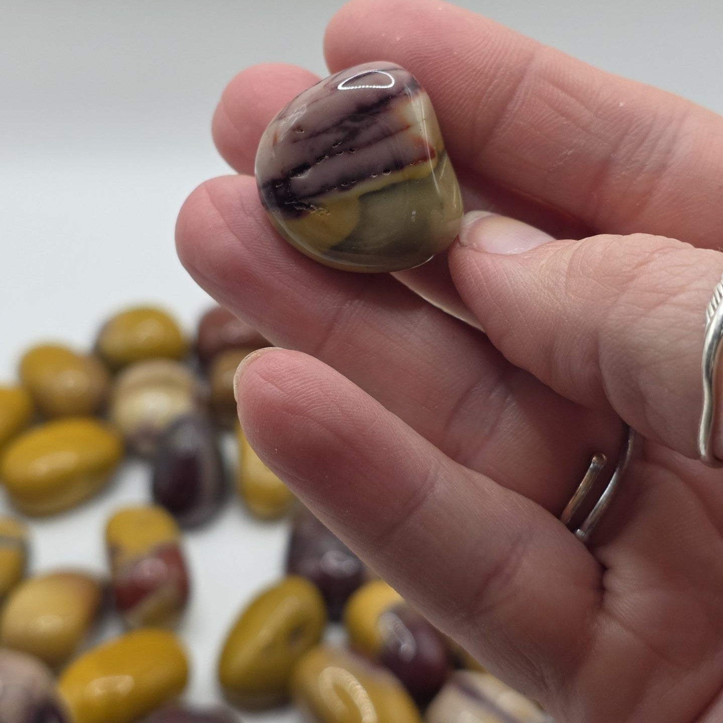 Hand holding a mookaite stone with more stones in the background on a neutral surface