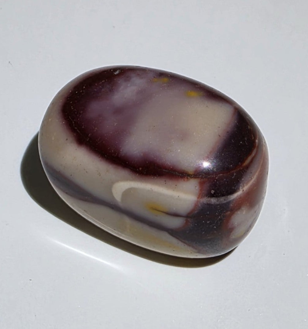 A Different Mookaite stone with purple, reds and white patterns on a plain background