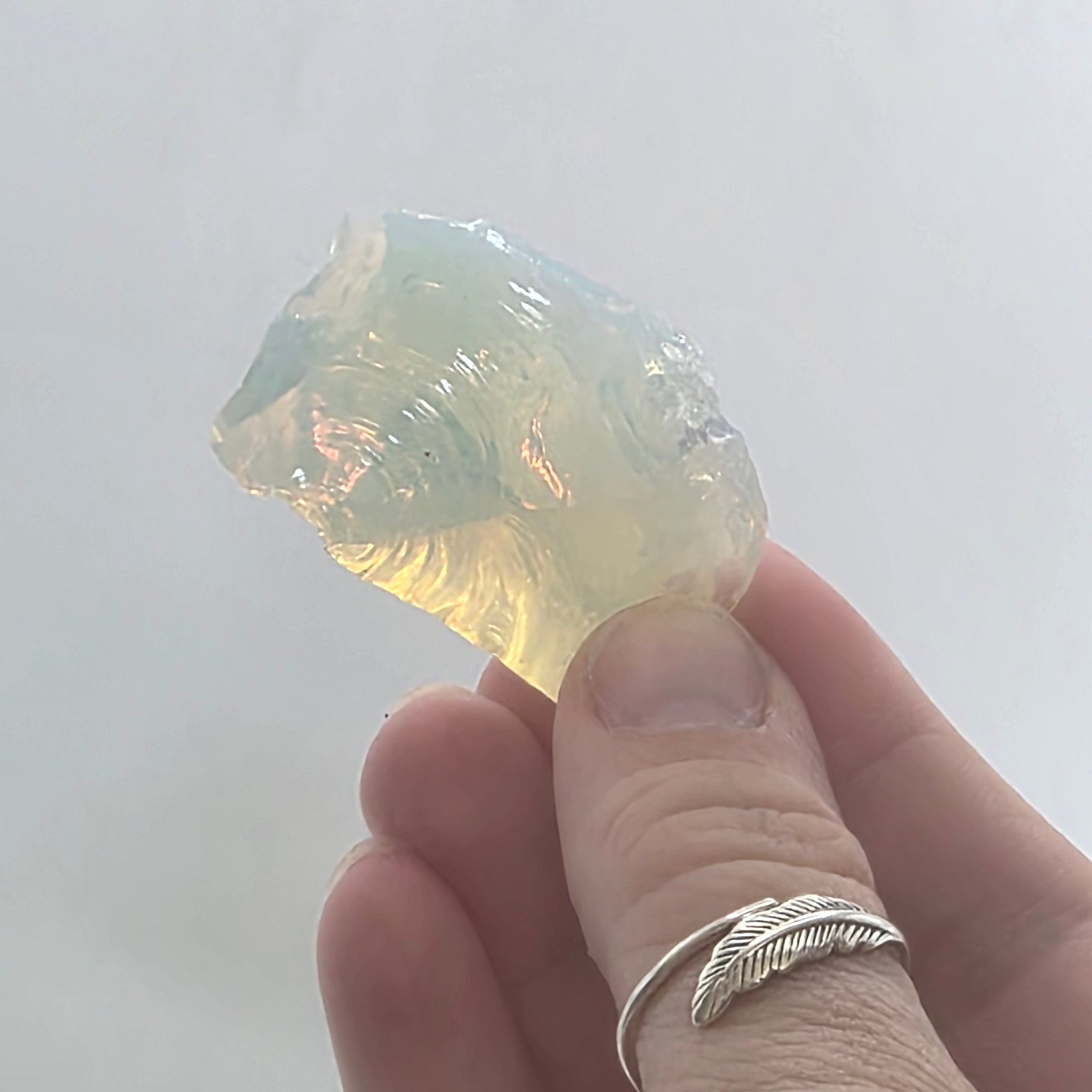 Hand holding a translucent opalite crystal reflecting against a white background