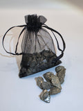 Black decorative bag with black ribbons next to small pyrite rocks on a white background
