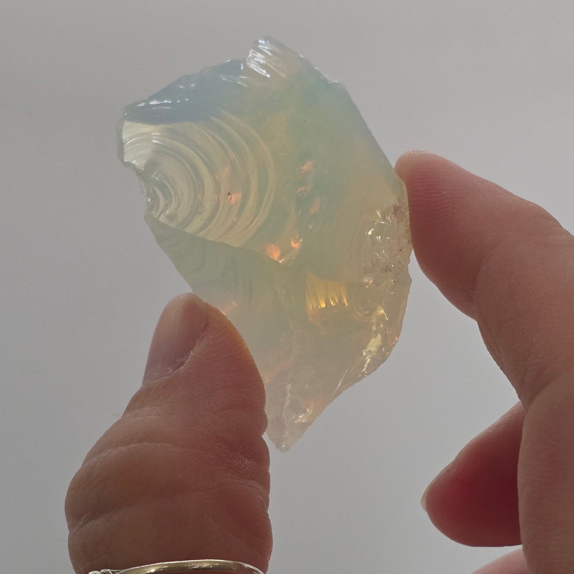 Hand holding a translucent opalite crystal against a plain background