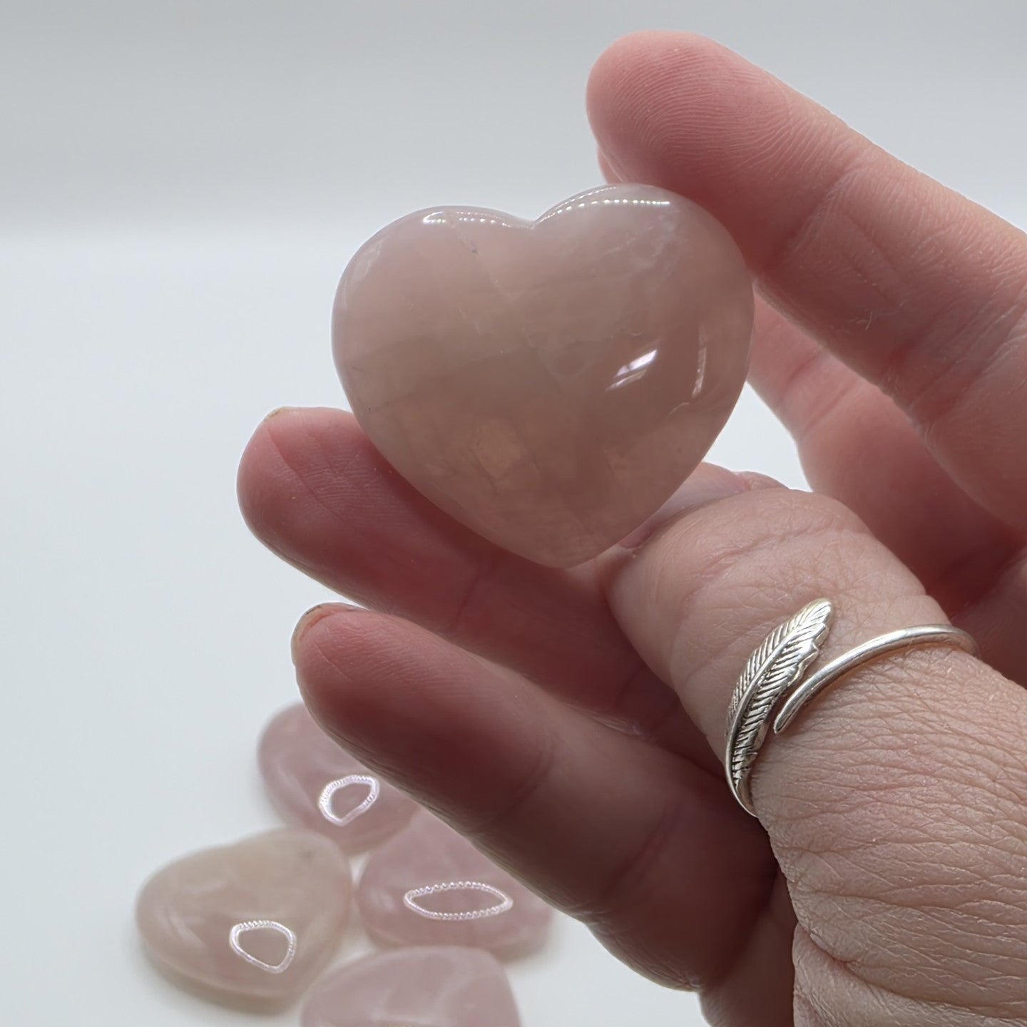 Heart-shaped rose quartz stone held between fingers with a plain background