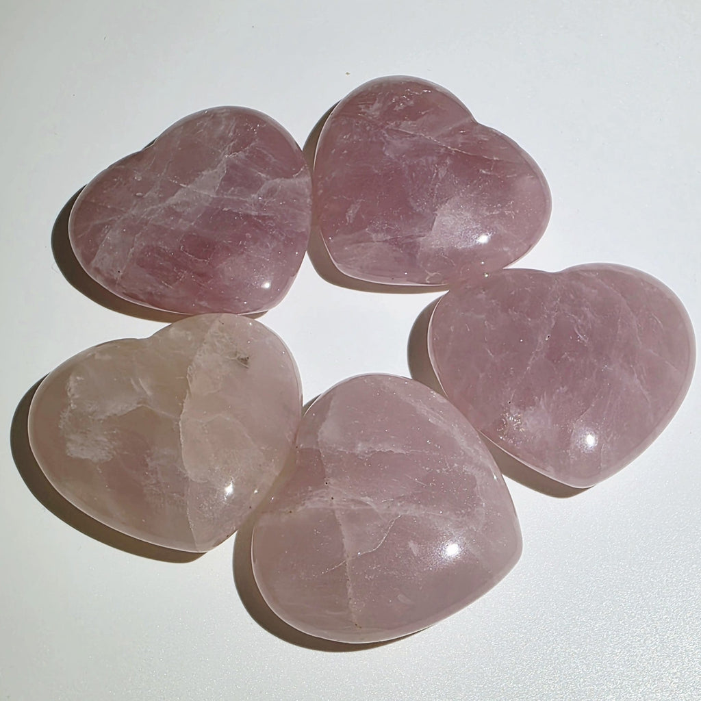 Five pink heart-shaped rose quartz crystals on a white background