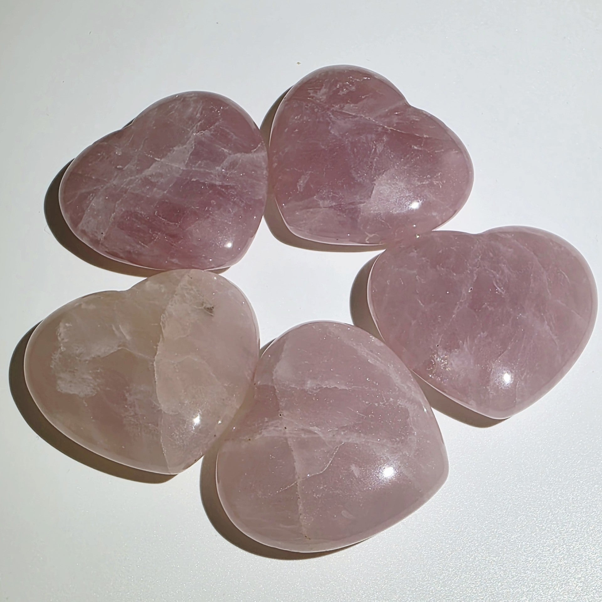 Five pink heart-shaped rose quartz crystals on a white background