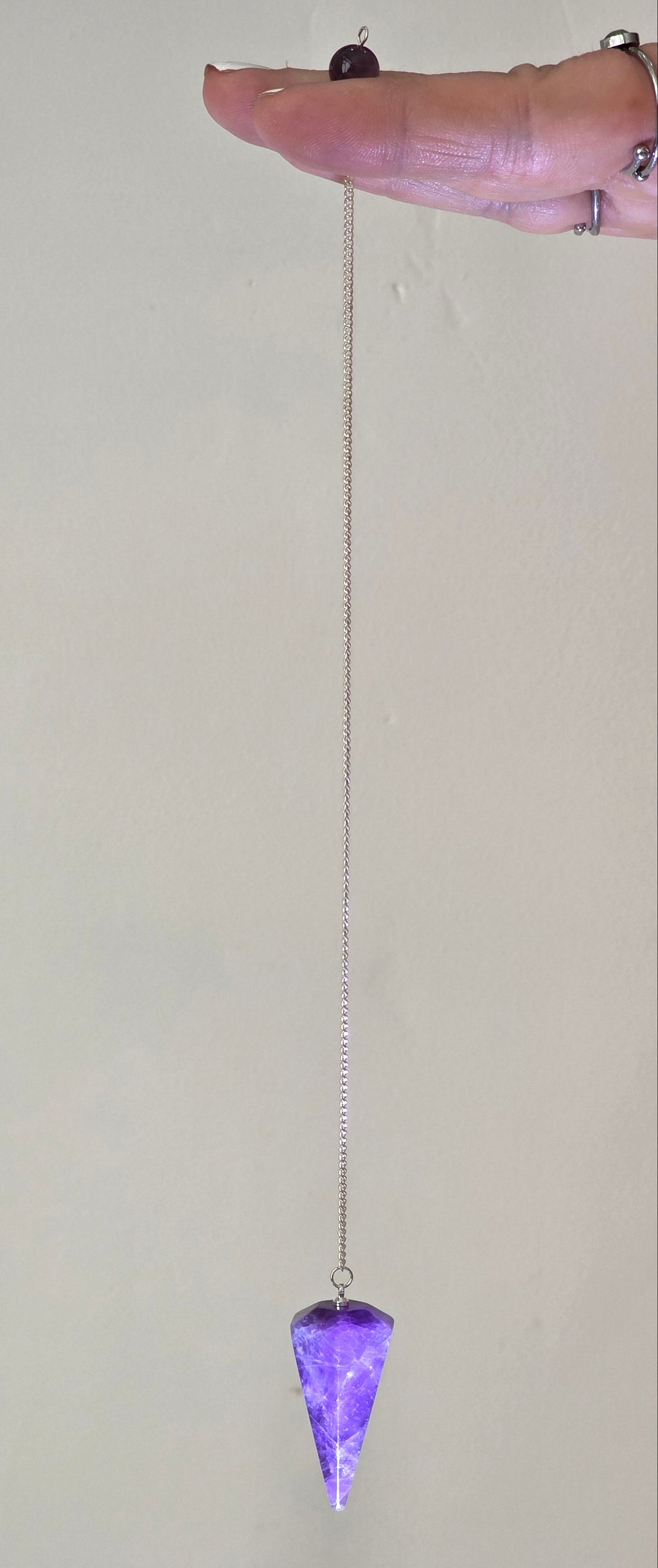 Amethyst pendulum held by the chain hanging freely in a person's hand