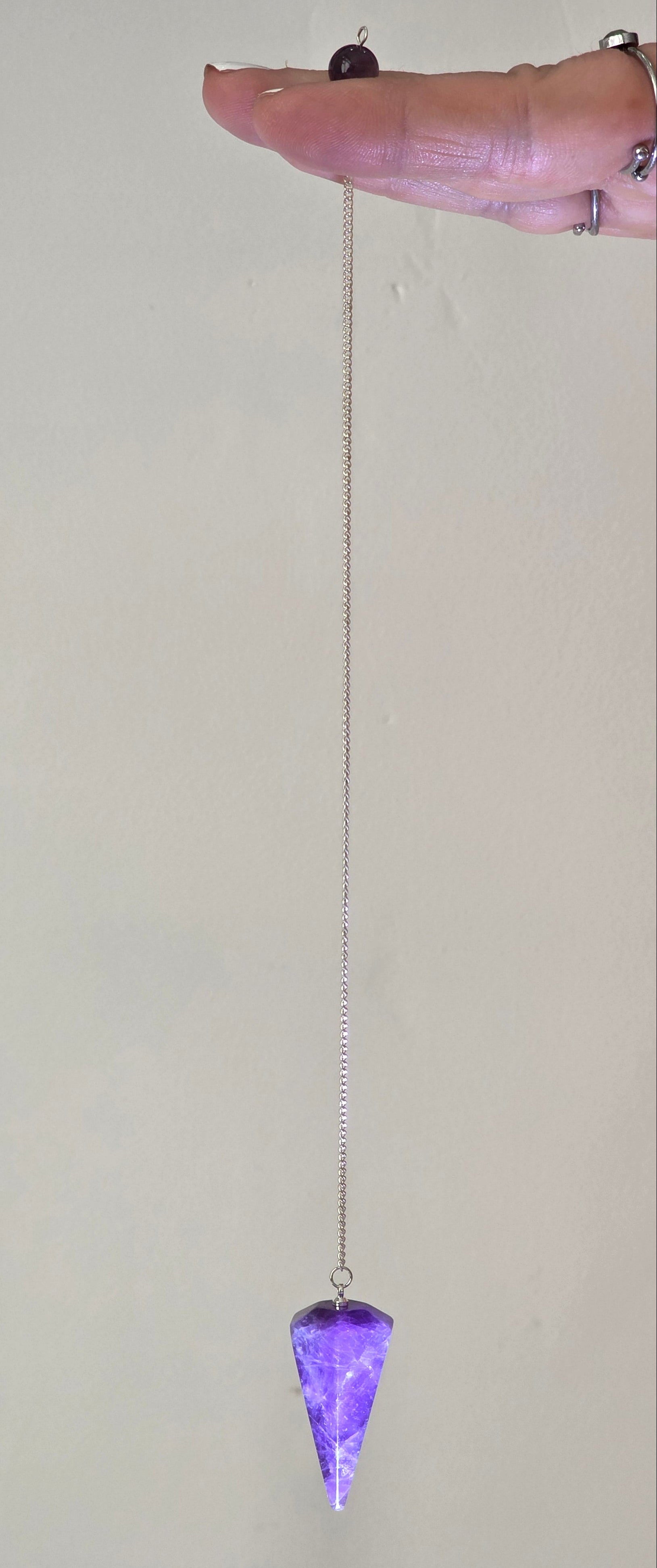 Amethyst pendulum held by the chain hanging freely in a person's hand