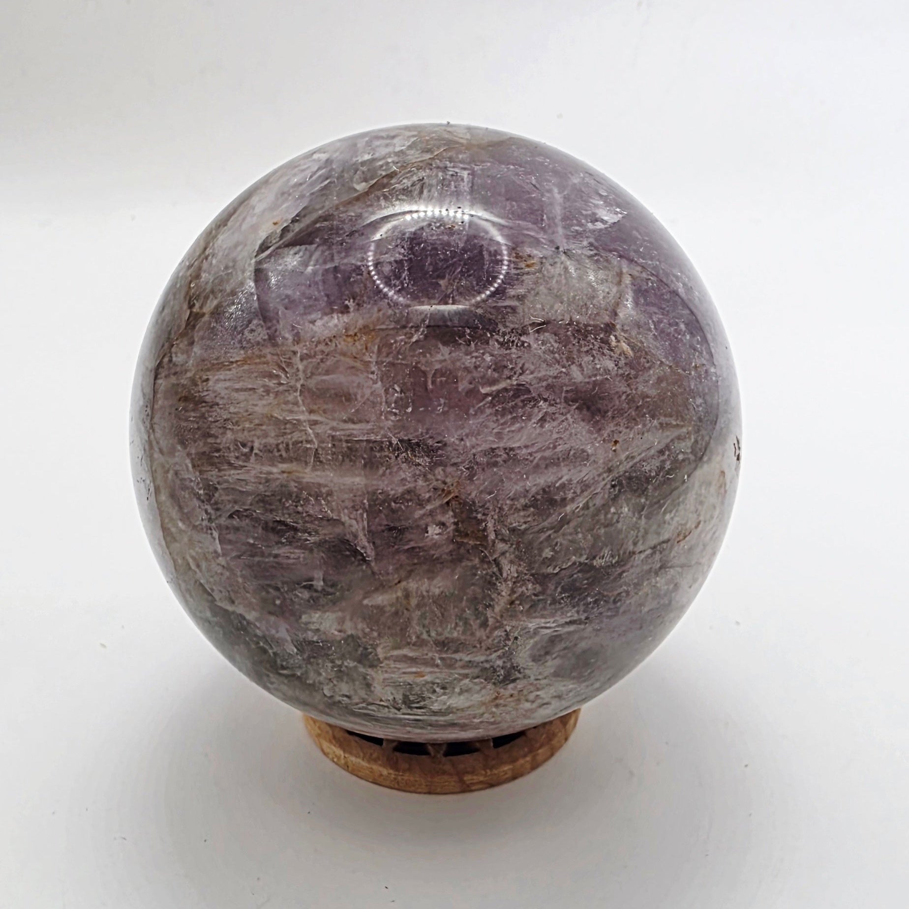 Polished amethyst crystal sphere with deep purple colour on white background