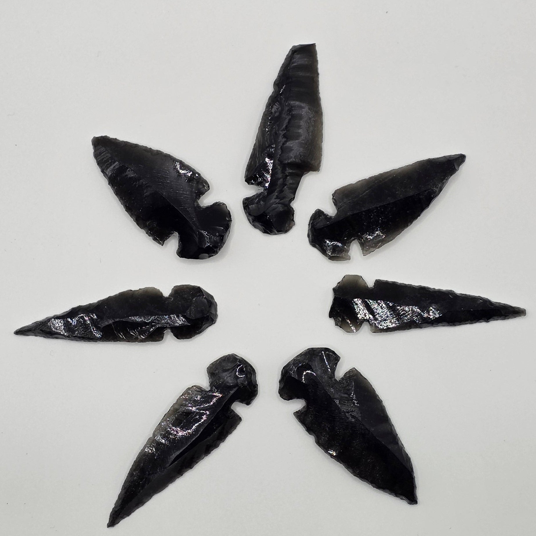 Variety of Hand-shaped black obsidian arrow heads in a circle on white background – natural volcanic glass from Mexico, 3-5cm long, glossy black