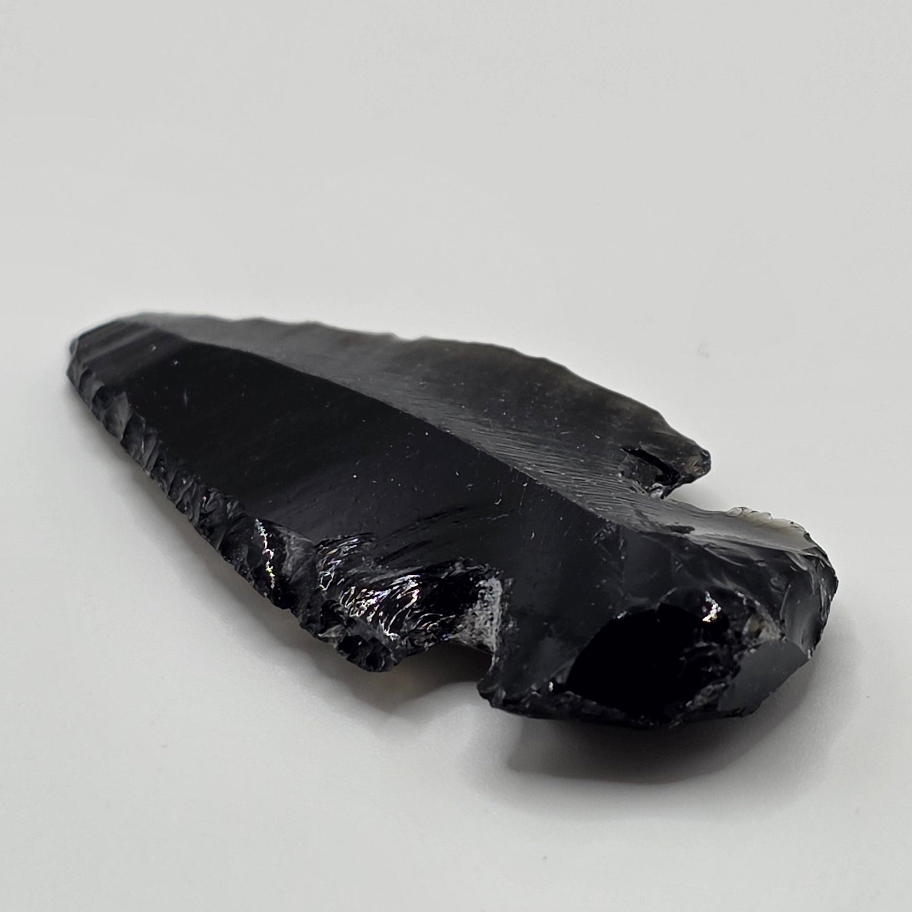 Hand-shaped black obsidian arrow head on white background – natural volcanic glass from Mexico, 3-5cm long, glossy black