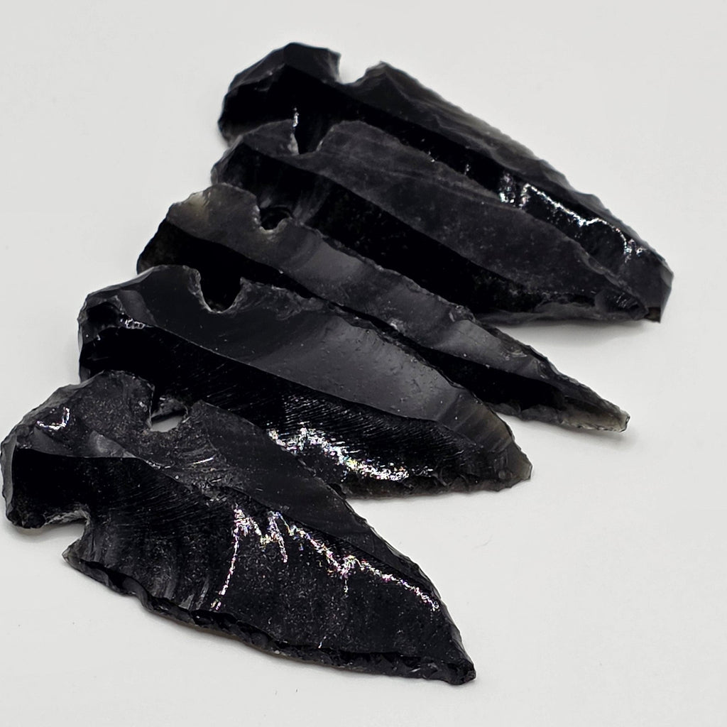 Variety of Hand-shaped black obsidian arrow heads in a row on white background – natural volcanic glass from Mexico, 3-5cm long, glossy black