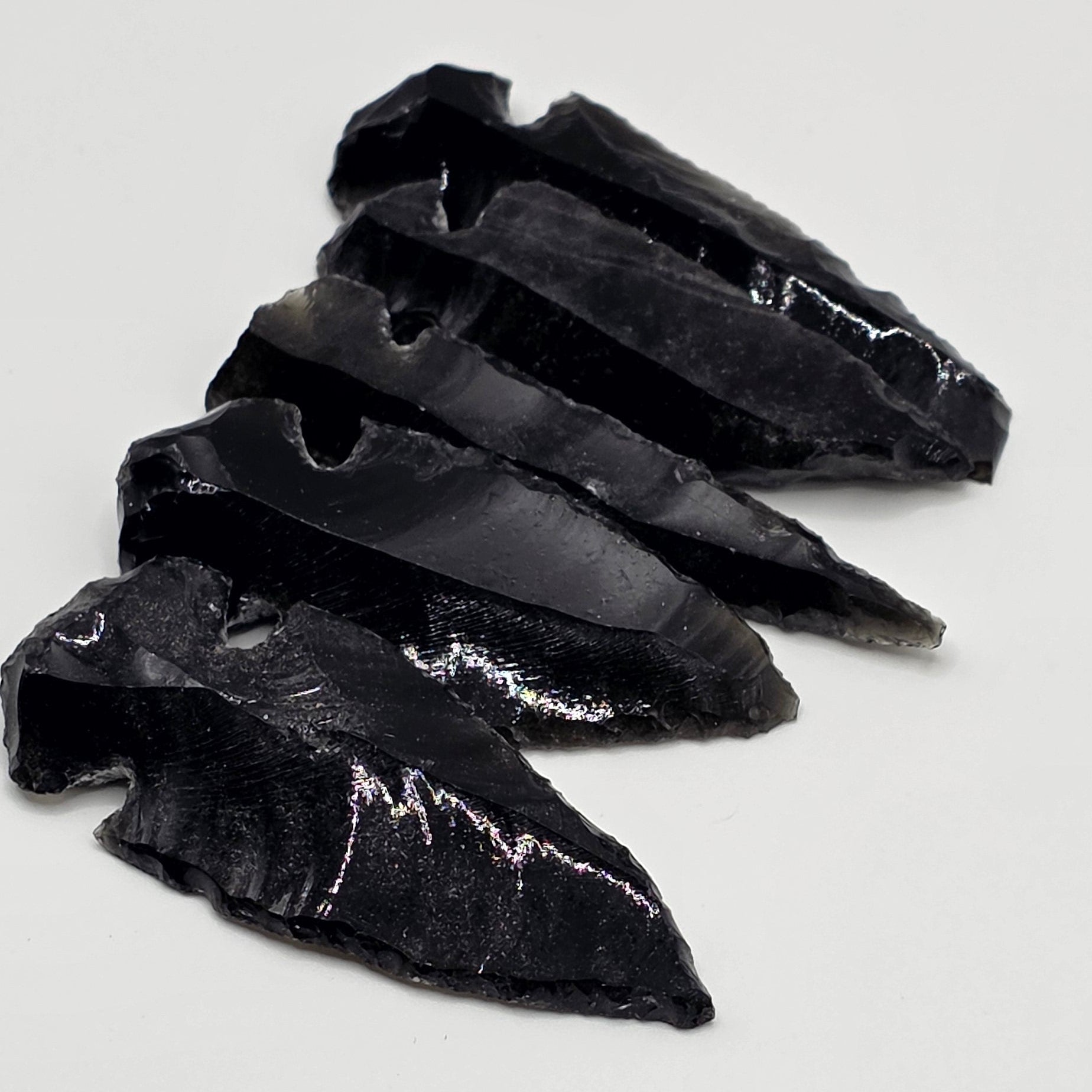 Variety of Hand-shaped black obsidian arrow heads in a row on white background – natural volcanic glass from Mexico, 3-5cm long, glossy black