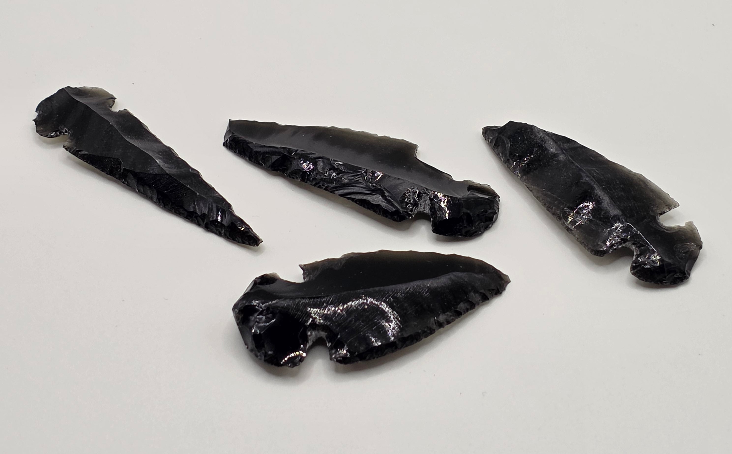 Variety of Hand-shaped black obsidian arrow heads on white background – natural volcanic glass from Mexico, 3-5cm long, glossy black