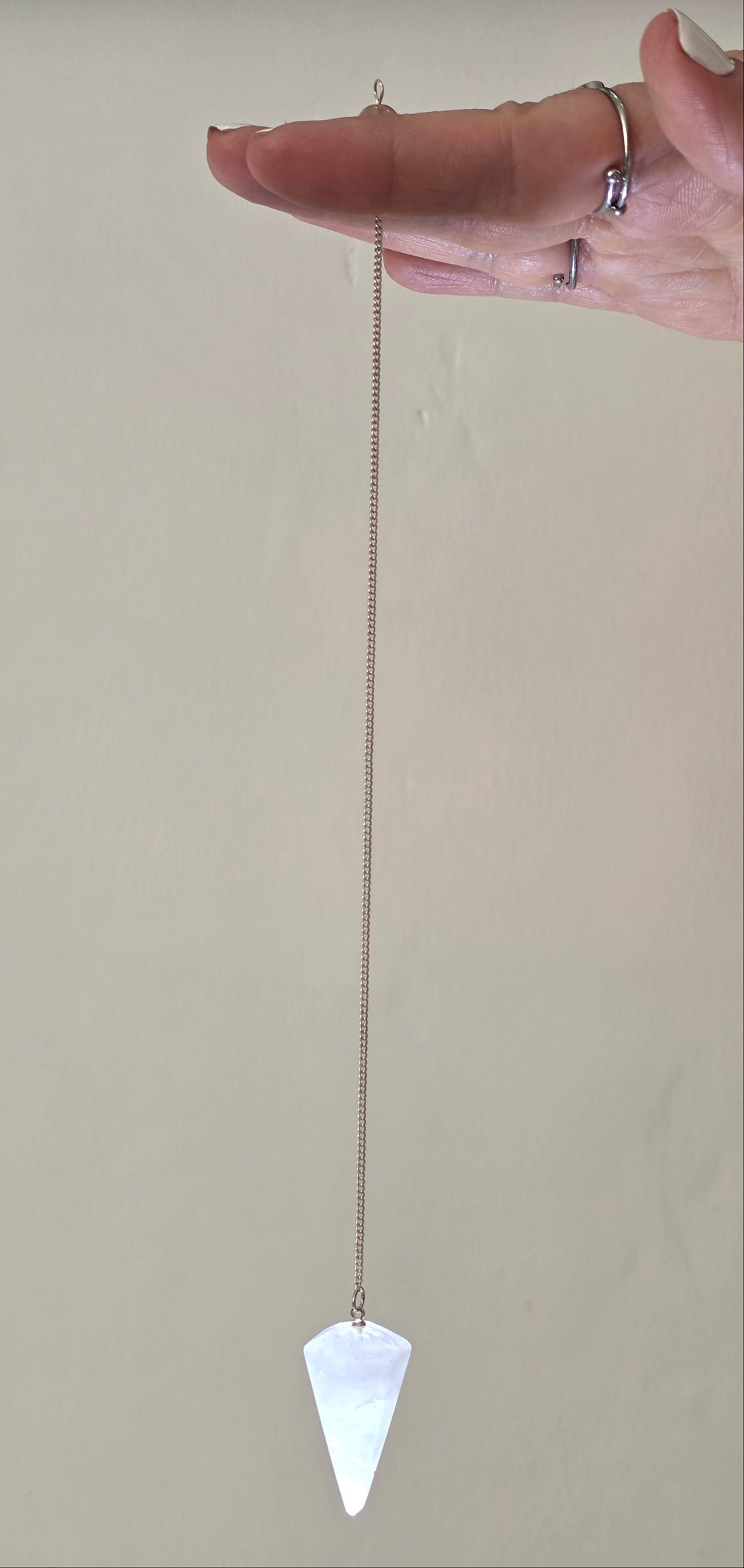 Clear quartz pendulum held by the chain hanging freely in a person's hand