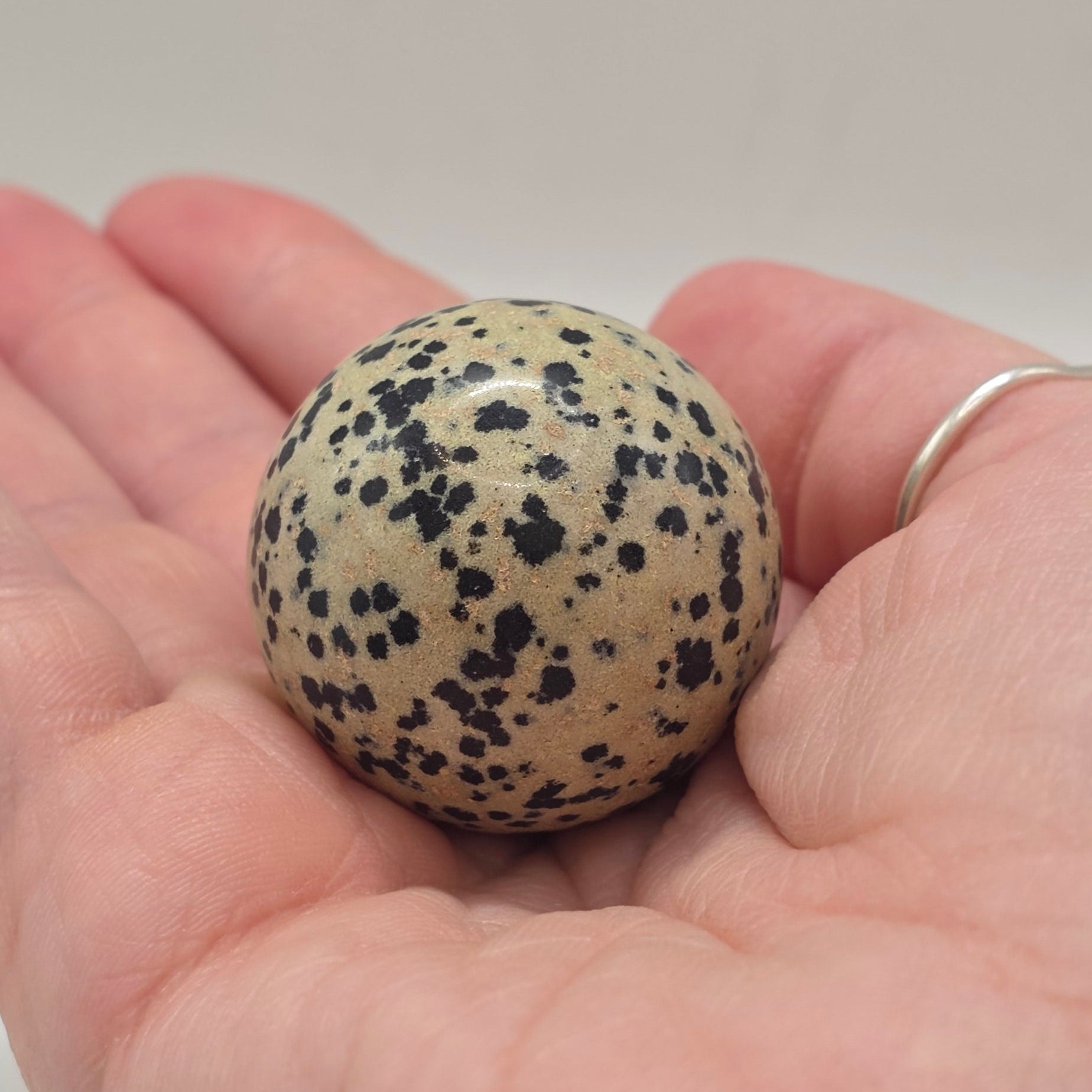 Dalmatian jasper sphere 35mm held in a person's hand – smooth polished crystal for inner child healing