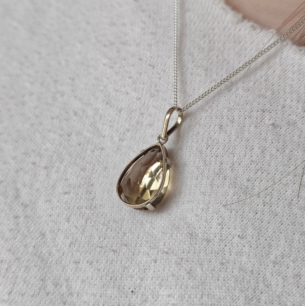 A  teardrop pendant necklace with a faceted citrine gemstone, resting on a textured light gray fabric surface.