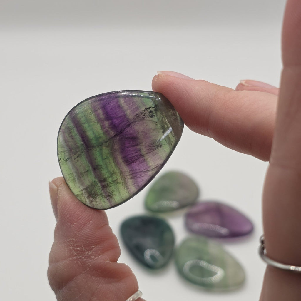 Hand holding Fluorite palm stone with more stones in the background on a white background
