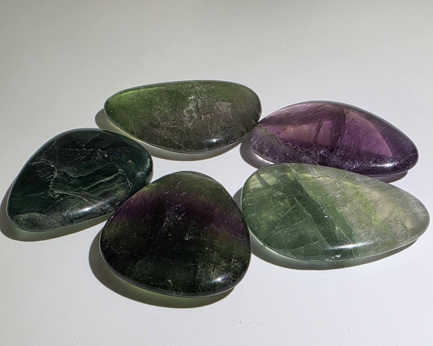 Five polished Fluorite in green and purple, laying flat on a white background