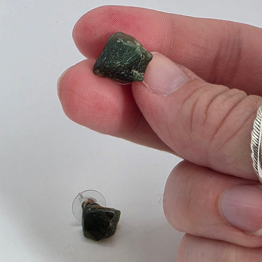 Hand holding a small green aventurine earring against a white background