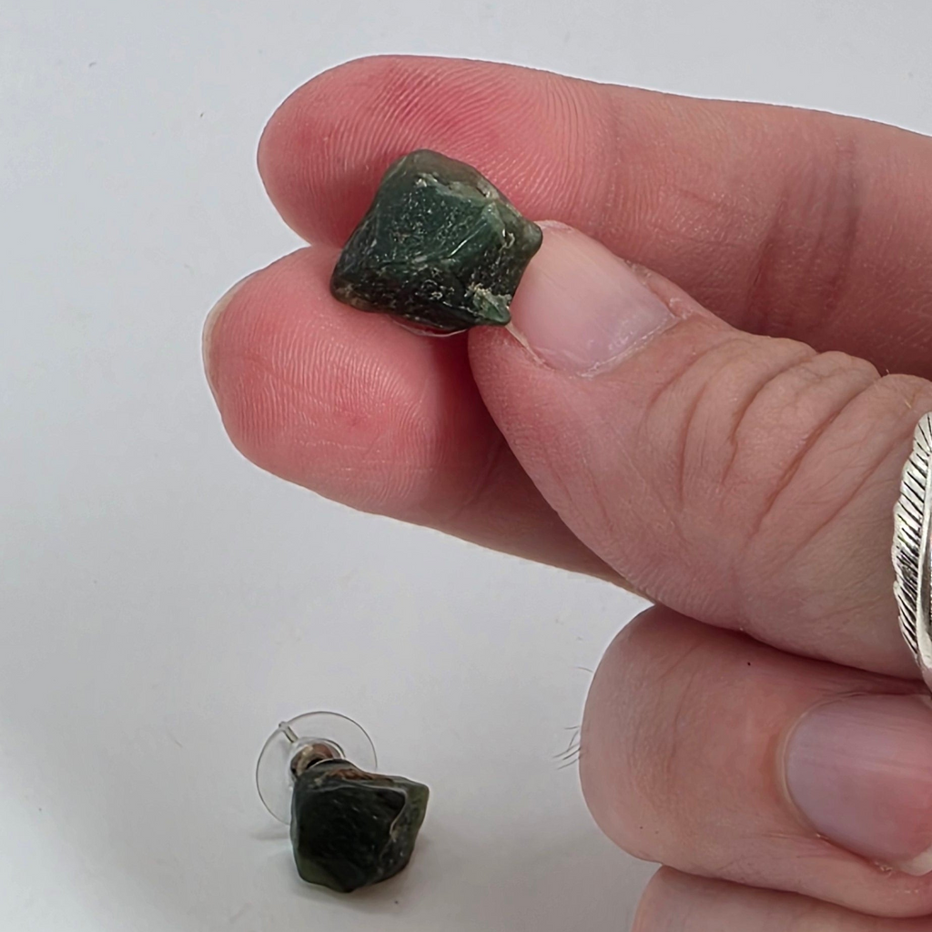 Hand holding a small green aventurine earrings with another on a white background