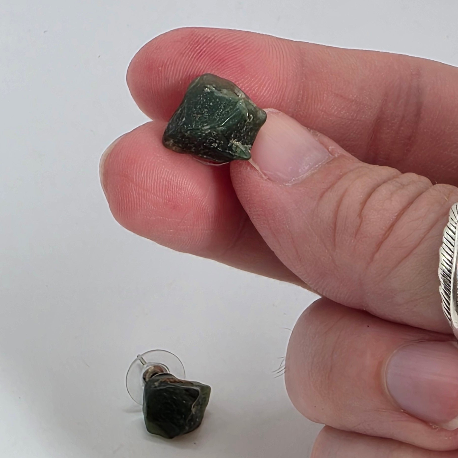 Hand holding a small green aventurine earrings with another on a white background
