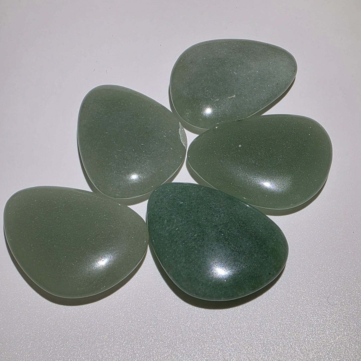 angled view of 5 green aventurine palm stones on a white background