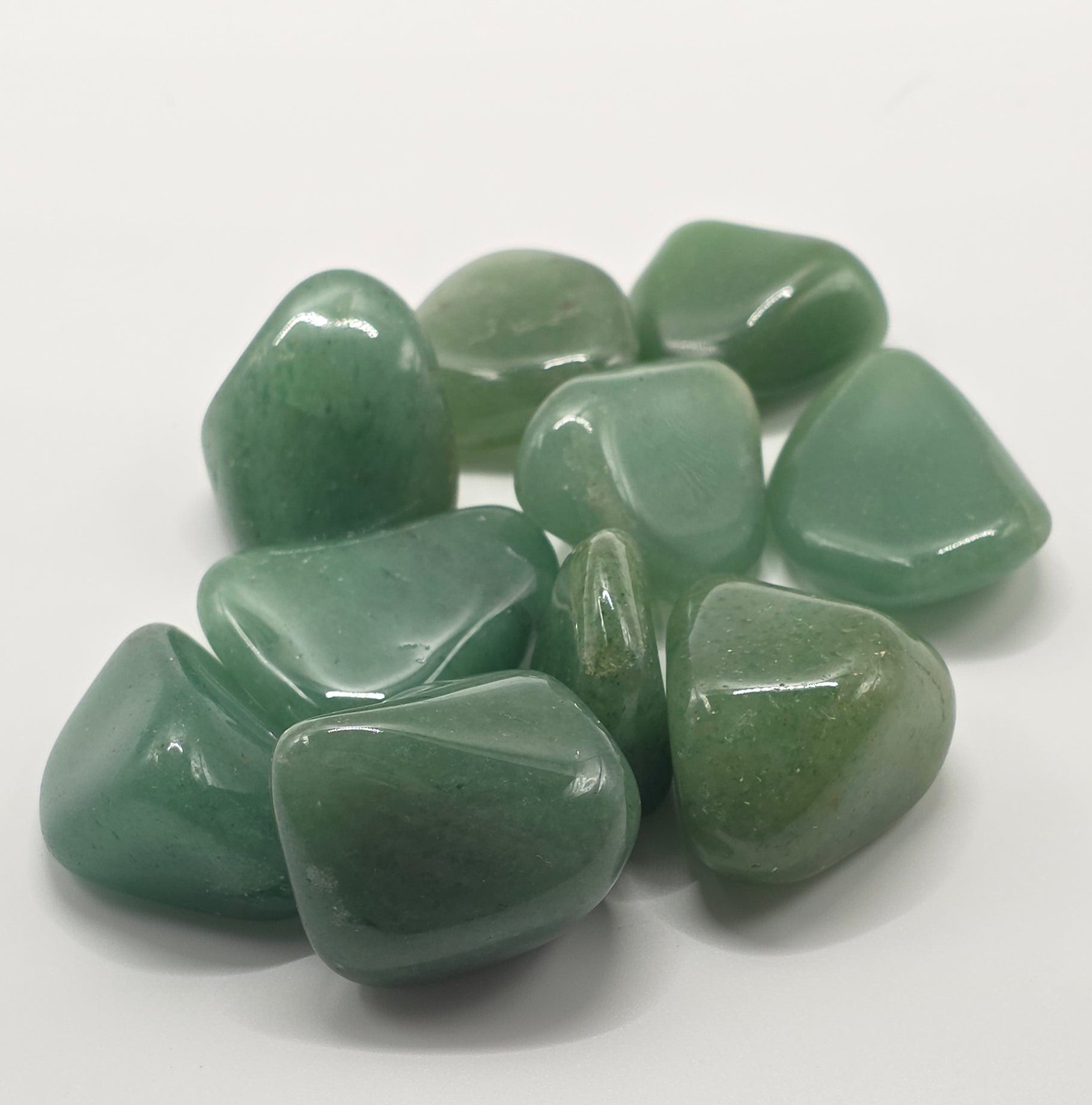 Overhead shot of Green aventurine tumbled stones on white background – dark green crystal for luck and opportunity