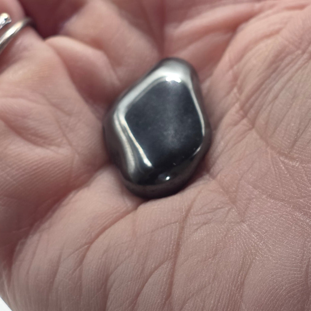 Hematite tumbled stone held in a person's hand – smooth polished crystal for grounding and anxiety relief