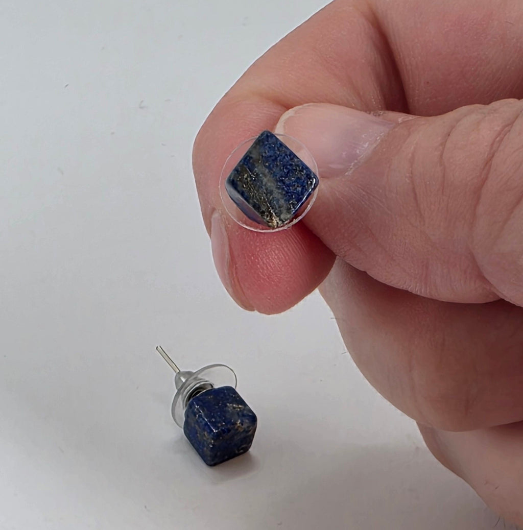 Hand holding a Lapiz earring with another one on a white surface