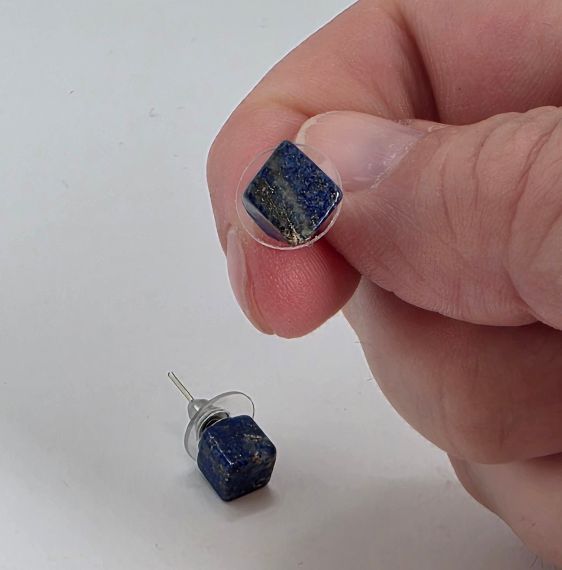 Hand holding a Lapiz earring with another one on a white surface