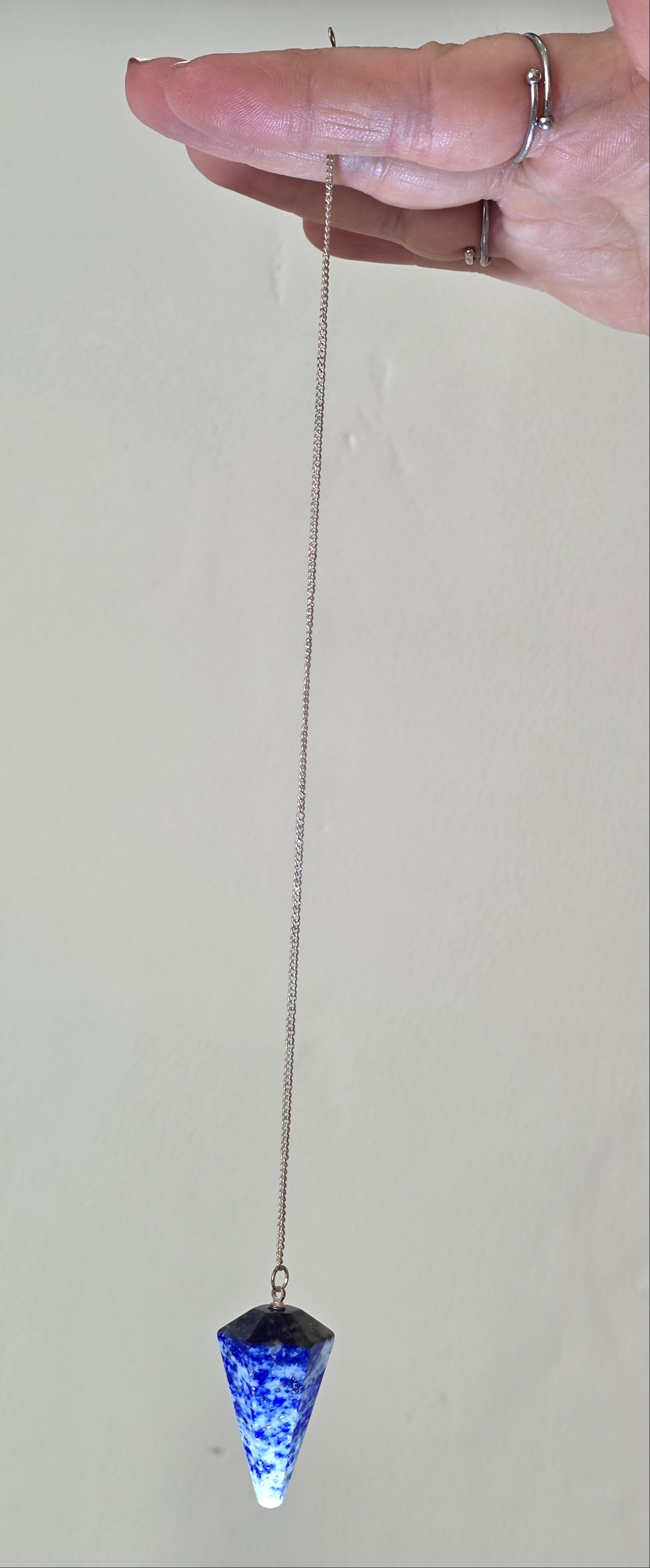 Lapis lazuli pendulum held by the chain hanging freely in a person's hand
