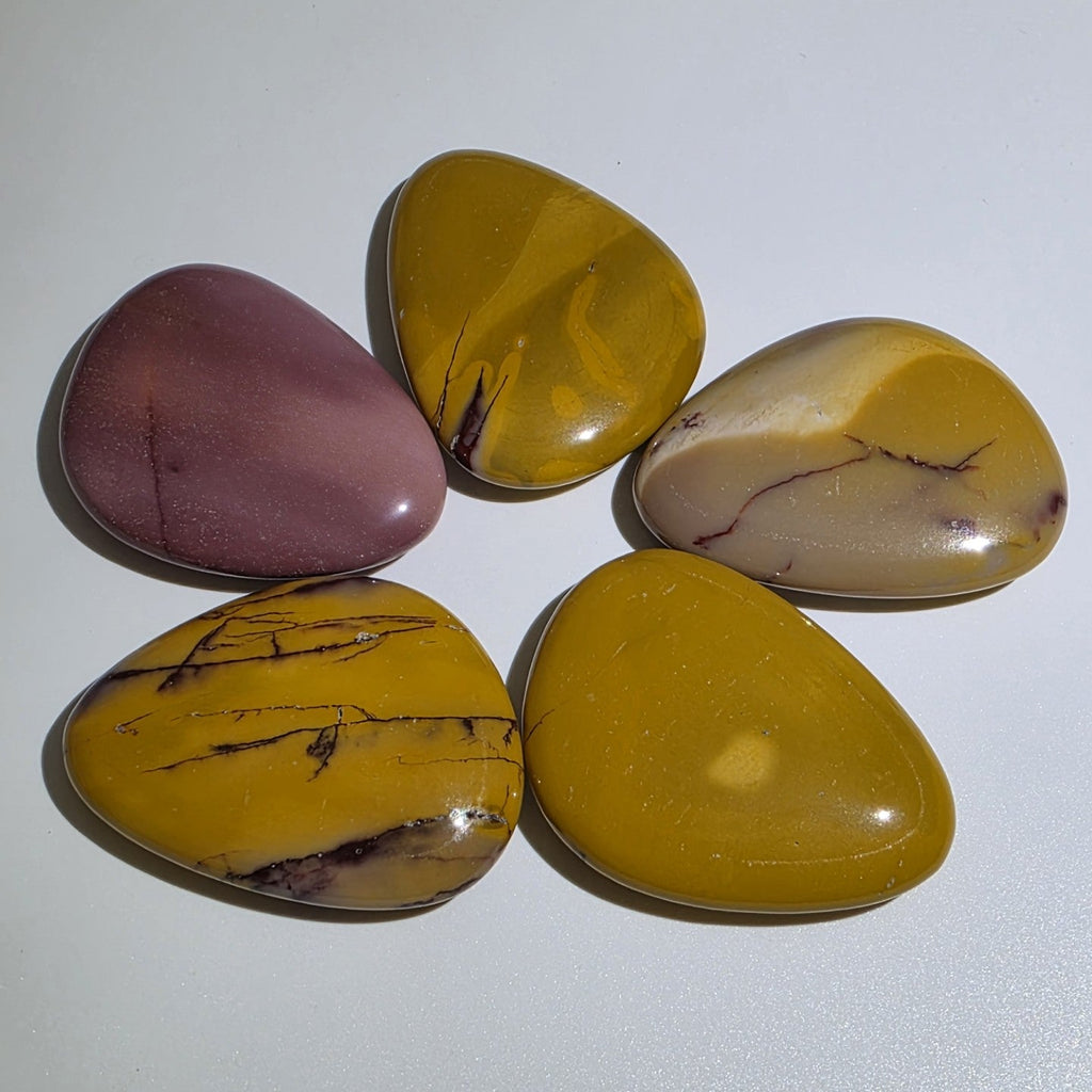 Five mookaite palm stones in yellow, brown, and purple on a white background