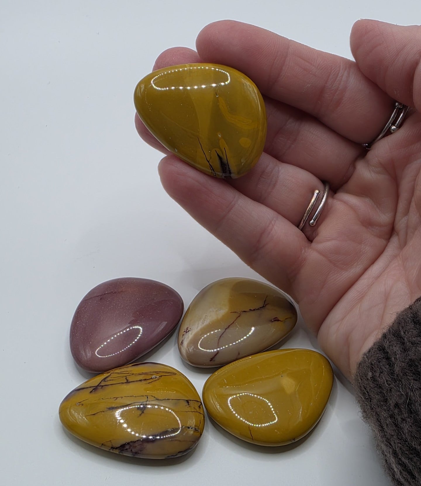 Hand holding mookaite palm stone with other stones on a white background